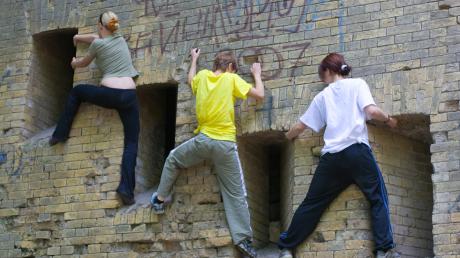 Drei Jugendliche hangeln eine Mauer entlang