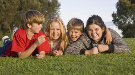 Vier Kinder liegen lachend auf der Wiese