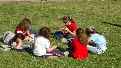 Kinder sitzen auf einer Wiese im Kreis und lesen