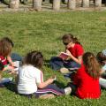 Sechs Mädchen sitzen im Kreis auf dem Rasen und lesen