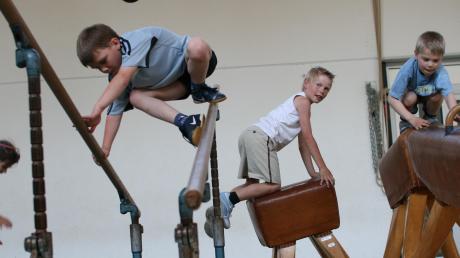 Vier Kinder turnen auf den Turngeräten Reck und Bock